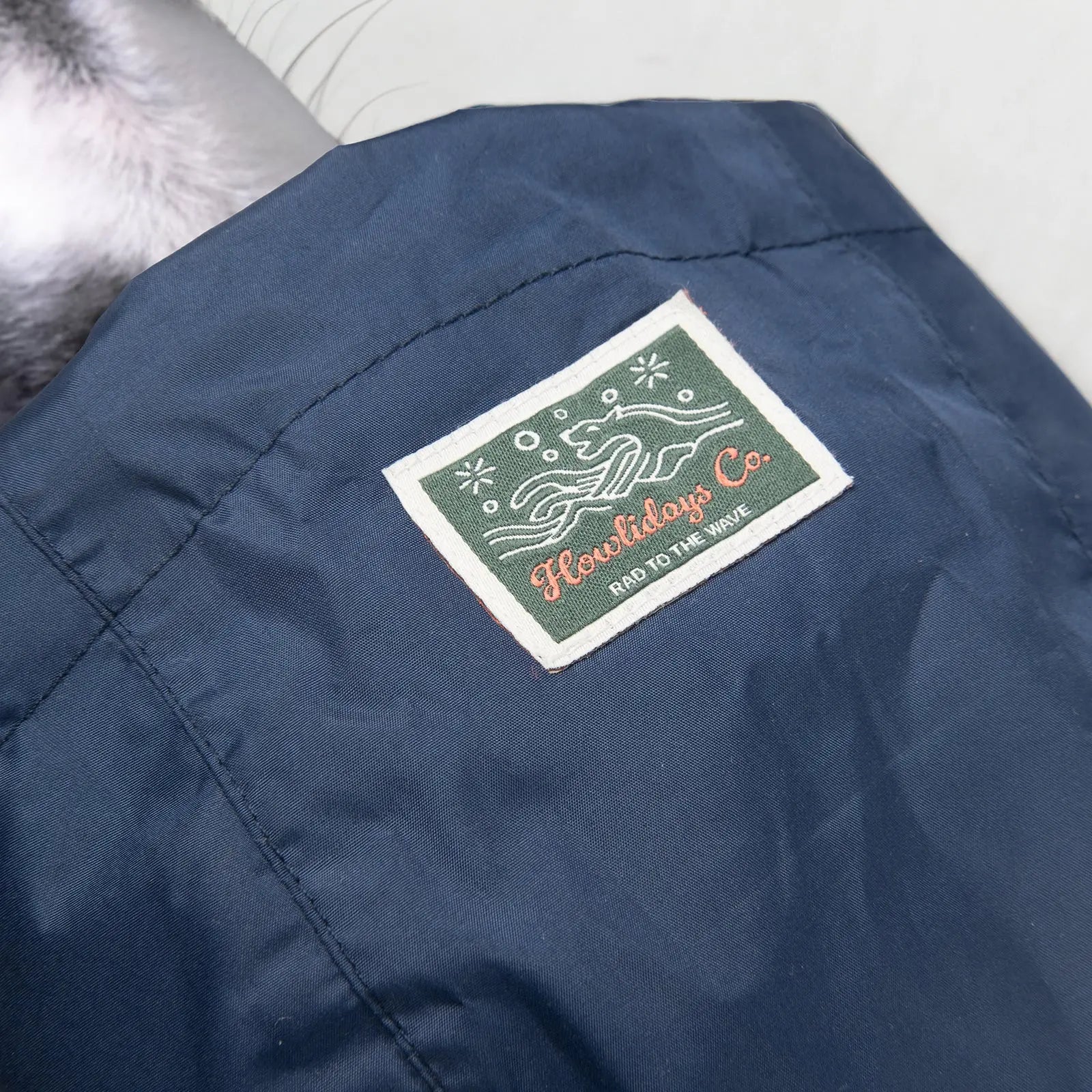 Close-up of the woven label on the Baja Coastline all-weather dog coat, featuring an ocean-inspired dog emblem with Howlidays Co. branding.